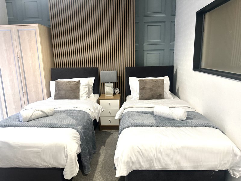 Twin bedroom with two single beds, white bedding, cushions, wooden headboard and bedside table