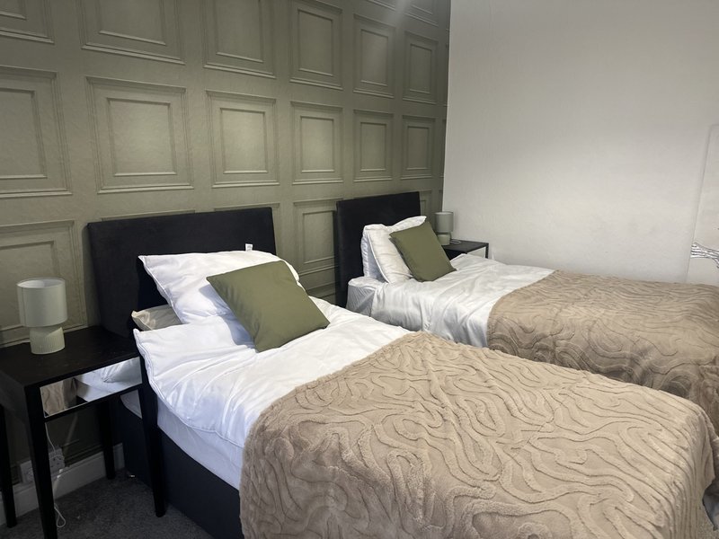 Twin bedroom with black headboards, white bedding, beige quilts and green cushions