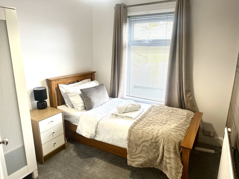 Bedroom with wooden bed frame, white nightstand, window with grey curtains and bedding