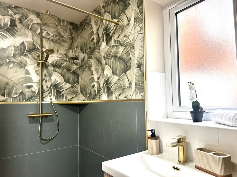 Modern bathroom with walk-in shower, botanical wallpaper, and white sink with brass fixtures