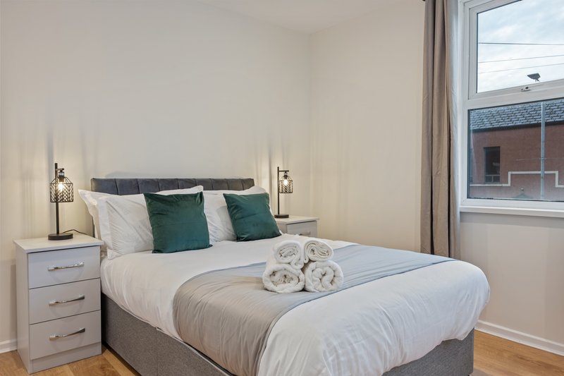 Modern bedroom with double bed, green pillows, white bedding, and bedside lamps