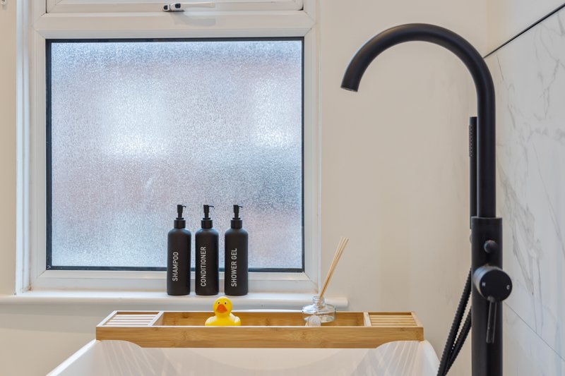 Modern bathroom with black faucet, wooden shelf, three black bottles, and frosted window