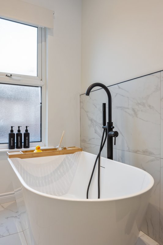 Modern bathroom with freestanding white bathtub, black faucet, and window with marble tiling
