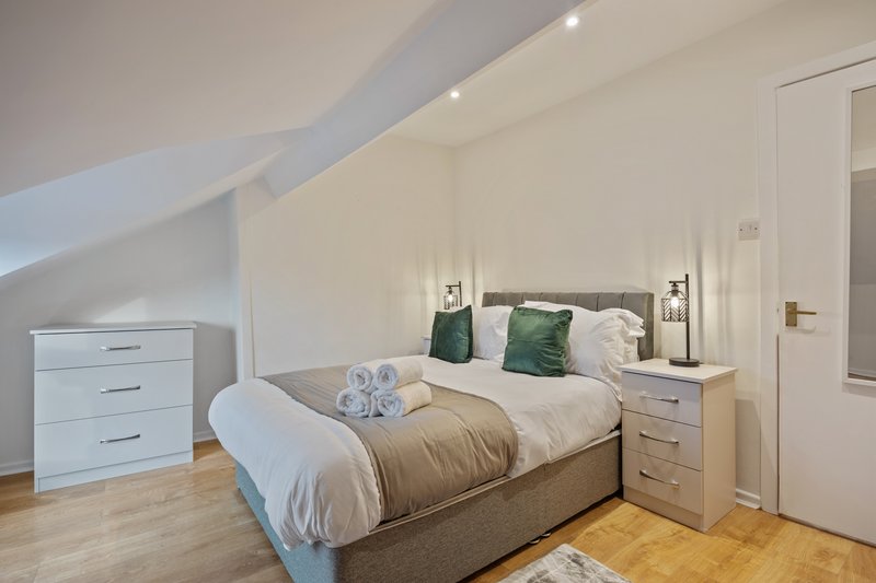 Attic bedroom with double bed, green pillows, wooden flooring and sloped ceiling