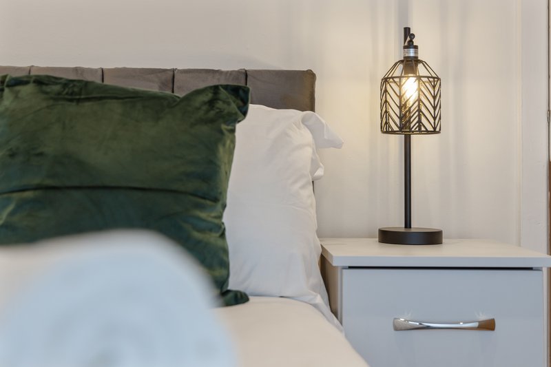 Bedroom with double bed, green and white pillows, bedside table and decorative lamp