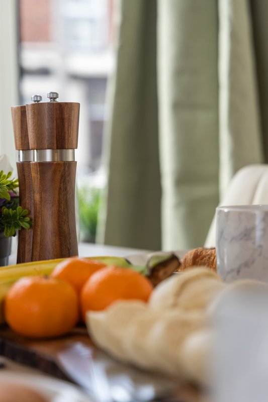 Kitchen counter with wooden pepper mill, fresh oranges, bread, and green plant by window