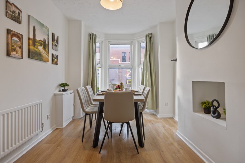 Bright dining room with round table, chairs, large bay window, wooden flooring and framed wall art