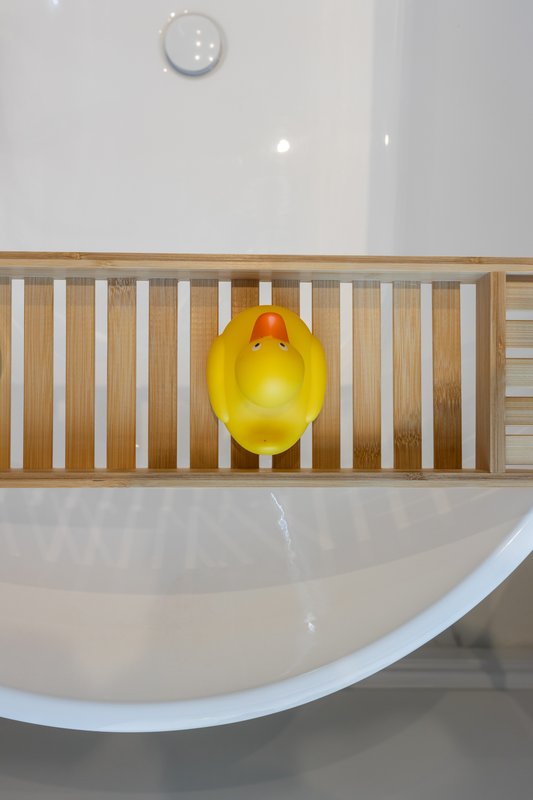 Modern bathroom with curved white bathtub, wooden bath caddy and yellow duck toy