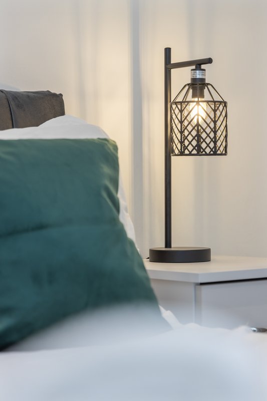 Bedroom with teal duvet, pillows, white nightstand and decorative black table lamp