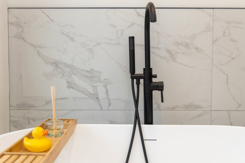Modern bathroom with white marble tiles, black faucet, and wooden shelf with yellow accessories