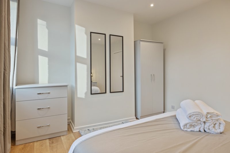 Bright modern bedroom with double bed, white dresser, mirrored wardrobe and wooden flooring
