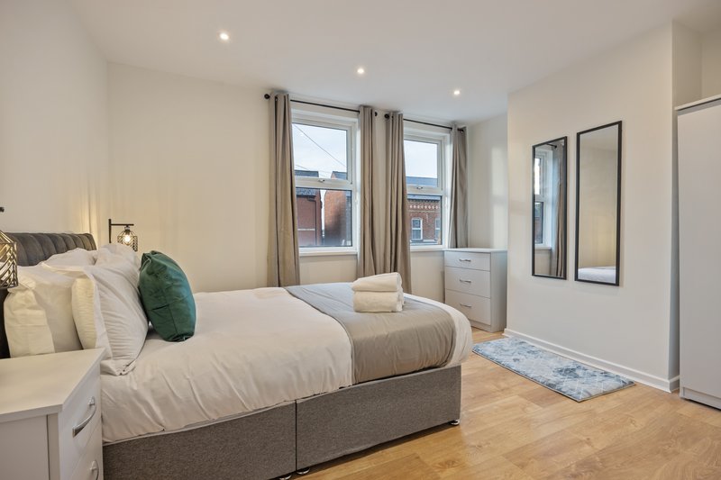 Modern bedroom with double bed, green cushion, wooden floor and large windows