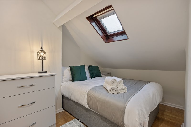 Attic bedroom with double bed, white bedding, green pillows, skylight window and white dresser