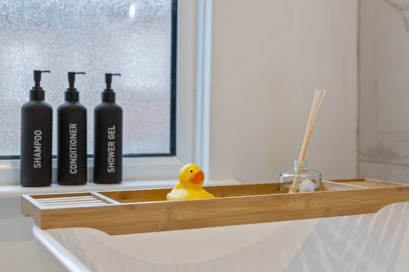 Bathroom shelf with toiletries bottles, yellow rubber duck, and reed diffuser by window