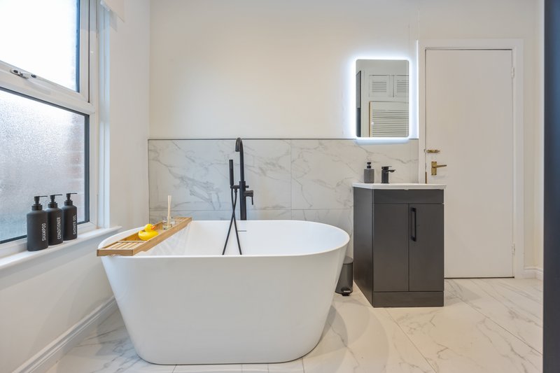 Modern bathroom with white freestanding bathtub, marble backsplash, dark vanity and window