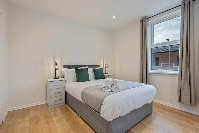 Modern bedroom with double bed, green cushions, wooden floor and window