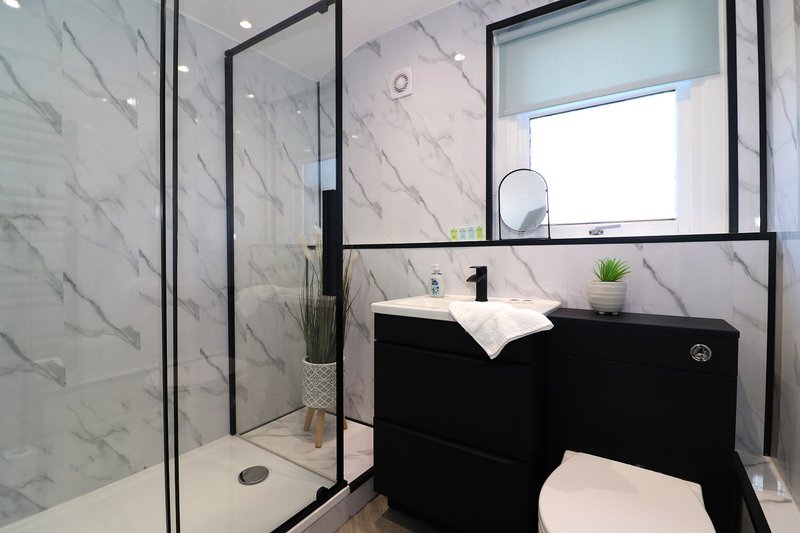 Modern bathroom with marble tile walls, black vanity, framed mirror and glass shower enclosure