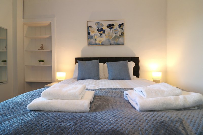 Modern bedroom with made bed, blue bedding, white pillows, wall art, and side lamps