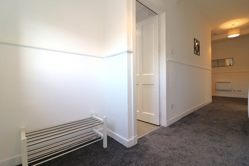 Empty room with white walls, dark carpet flooring, white door frame and minimal furniture