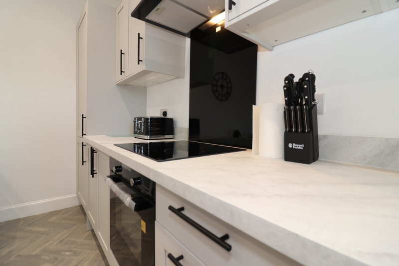 Modern kitchen with white cabinets, black splashback, built-in oven and knife block on countertop