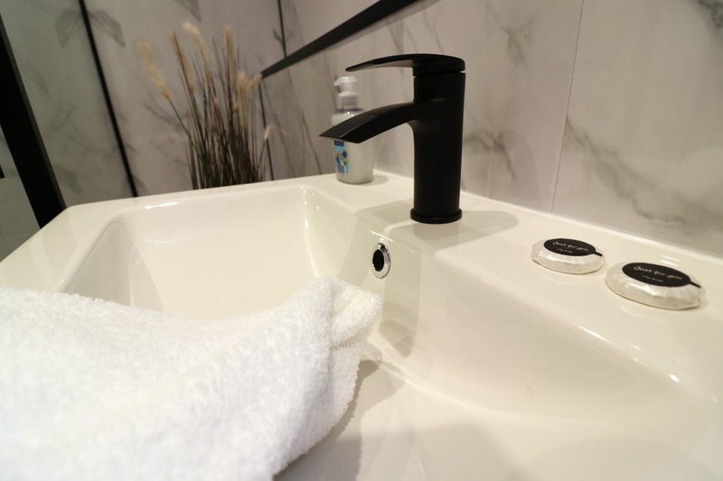 Modern white bathroom sink with black faucet, folded towel, and decorative plant