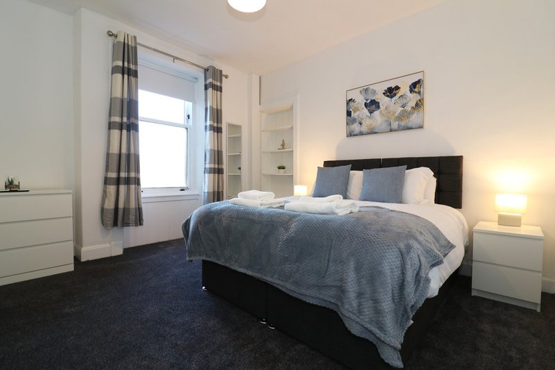 Modern bedroom with double bed, bedside tables, window with checked curtains and wall art