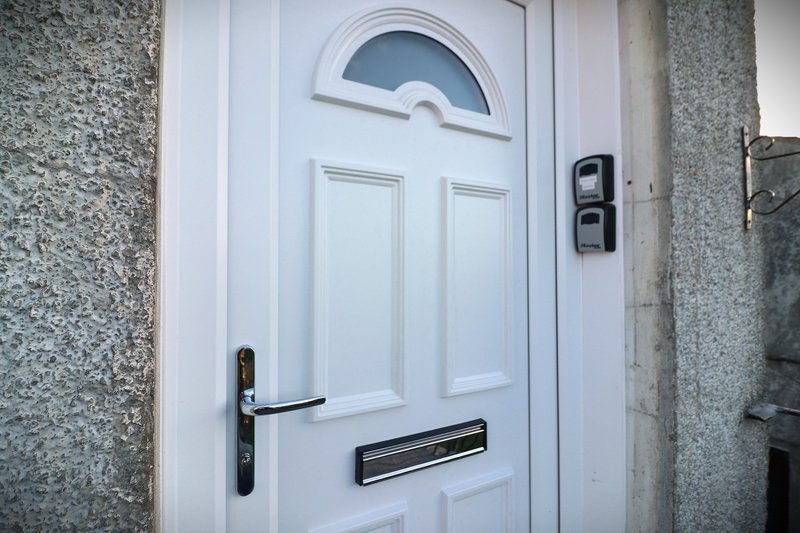 White front door with arched transom window, black handle and letterbox on gray stone exterior