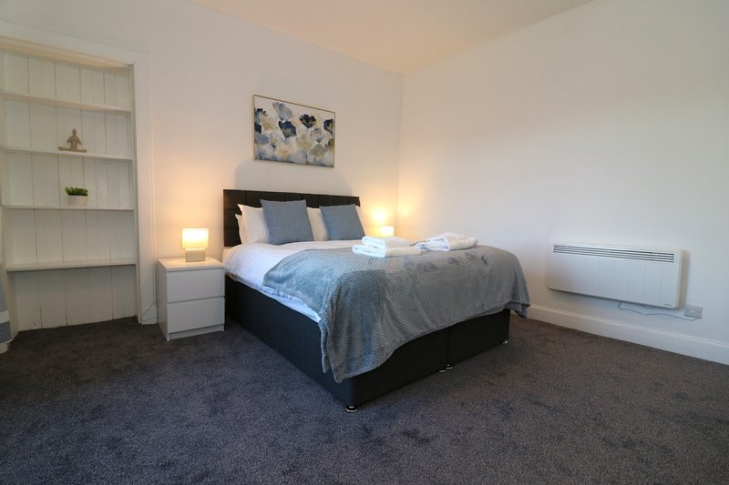 Spacious bedroom with double bed, bedside lamps, shelving unit and dark carpet flooring