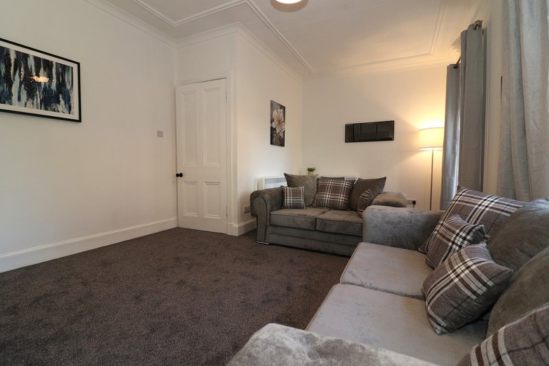 Living room with grey sofa, armchair, brown carpet, white walls and door