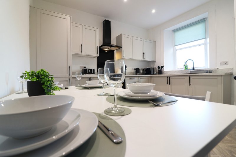 Modern kitchen with white cabinetry, island with place settings, and black range hood