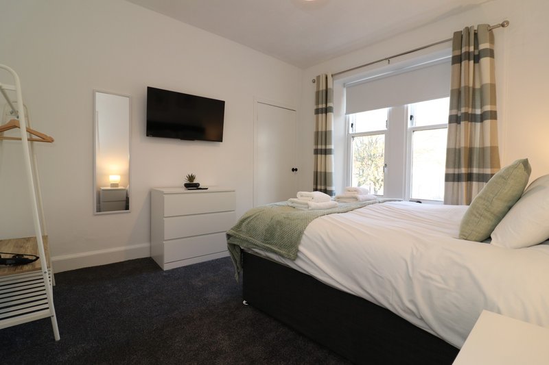 Modern bedroom with double bed, wall-mounted TV, white dresser and patio doors