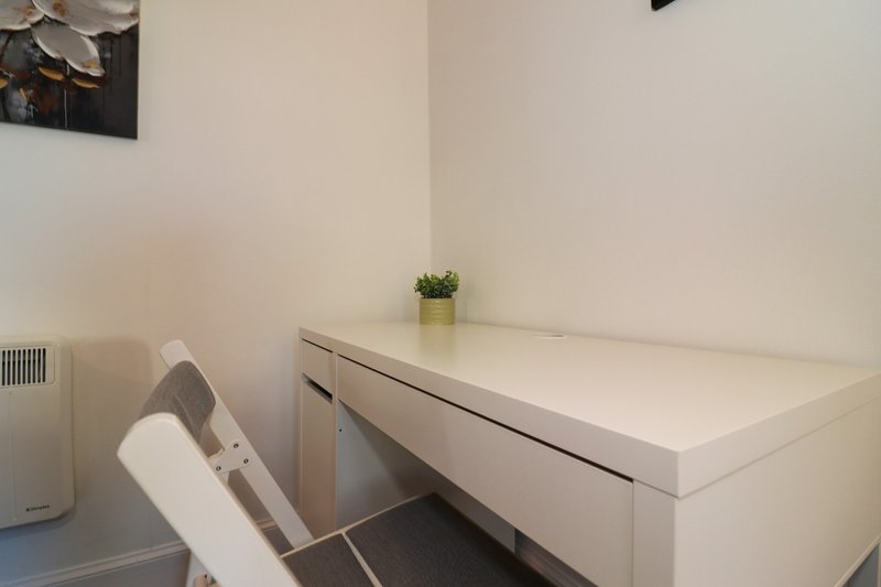 Modern home office with white desk, office chair, small plant and radiator