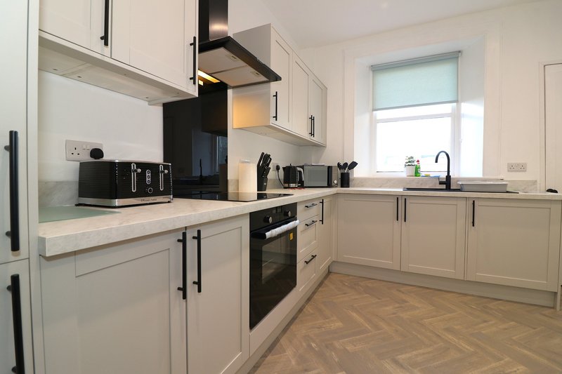 Modern kitchen with cream cabinetry, black appliances, light countertops and wooden flooring