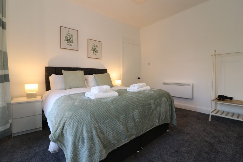 Bedroom with double bed, bedside lamps, framed botanical prints, and white storage furniture
