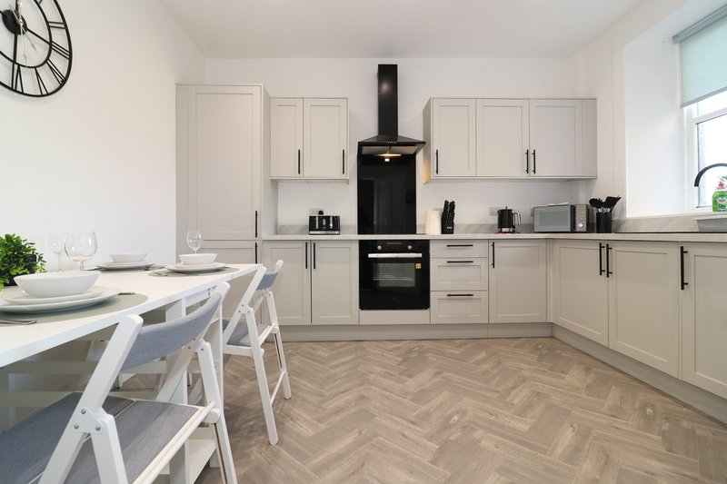 Modern kitchen with cream cabinets, black cooker hood, dining table and white chairs