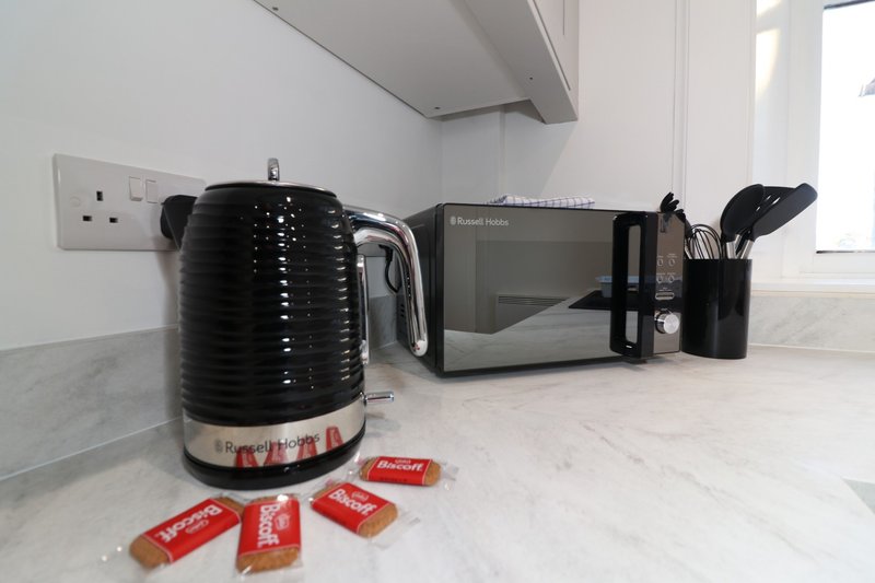 Kitchen counter with black kettle, microwave, utensil holder and packaged food items