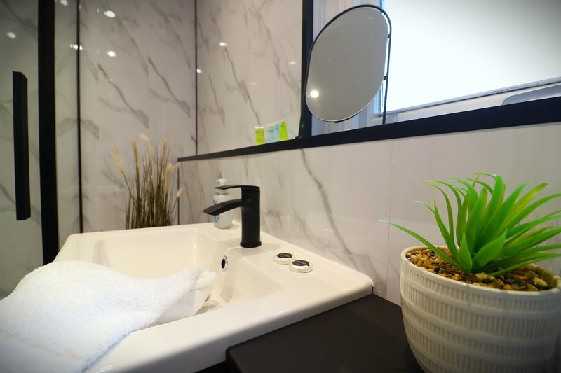Modern bathroom with white basin, black tap, round mirror and potted plants
