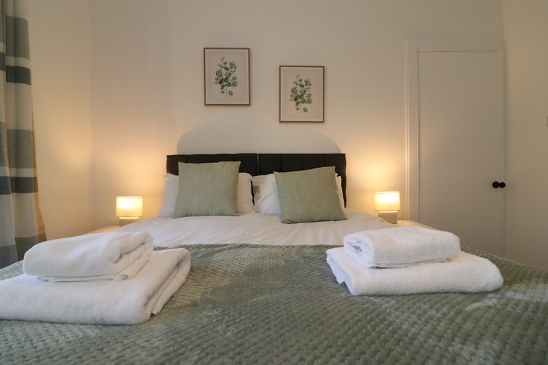 Bedroom with double bed, green bedding, white pillows, wall art, and bedside lamps