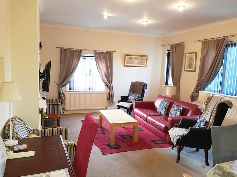 Spacious living room with red sofa, armchairs, wooden table and multiple windows with curtains