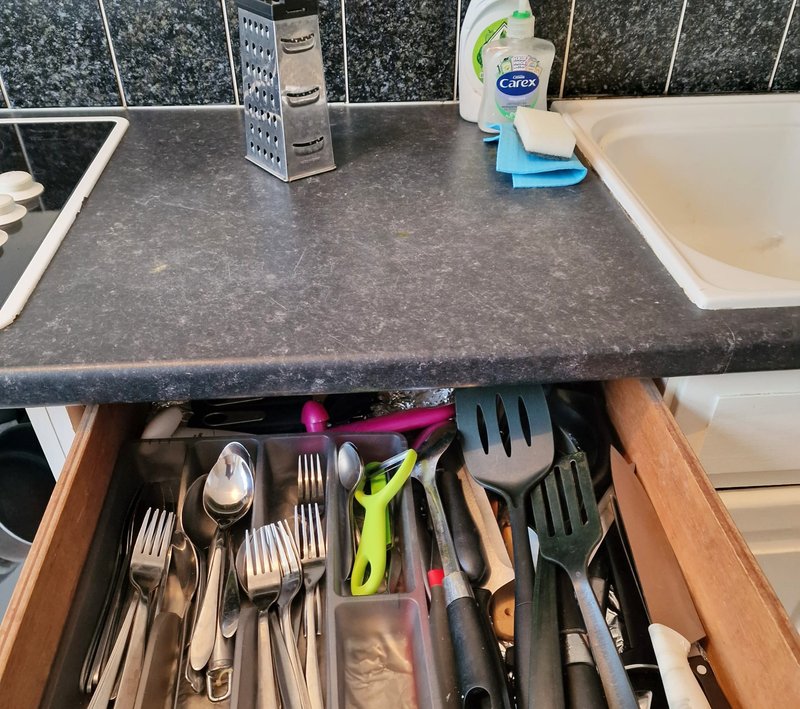 Kitchen drawer open showing cutlery, utensils and cooking tools with countertop and backsplash visible
