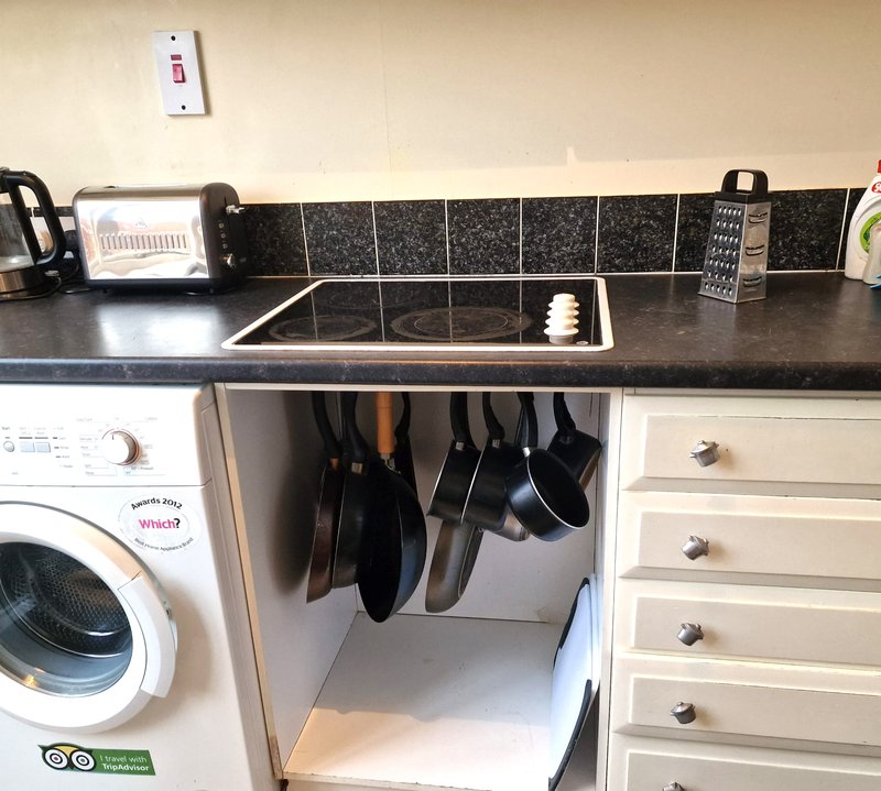 Kitchen counter with washing machine, sink, cooktop, and hanging cookware