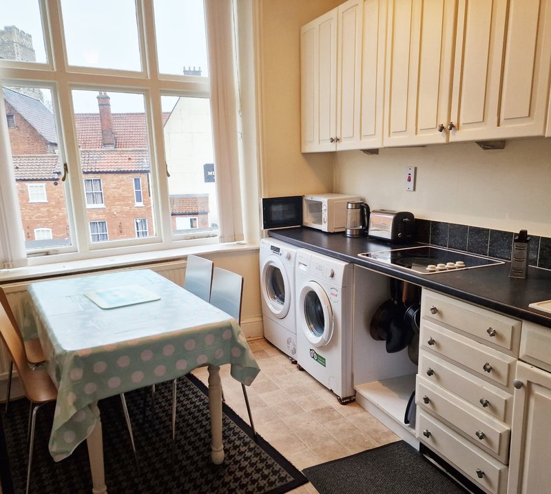Kitchen with cream cabinets, black countertop, washing machines, dining table and large window overlooking street