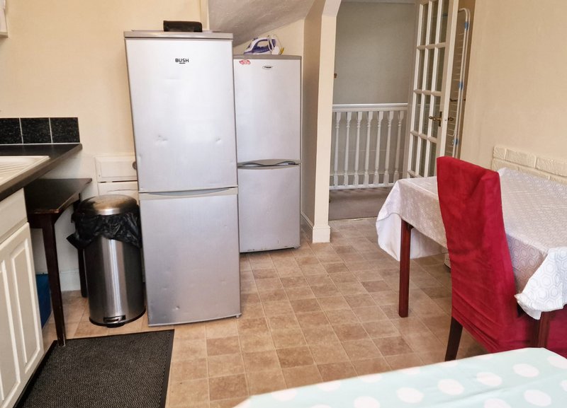 Kitchen and dining area with refrigerators, kettle, table with red chair and white towel