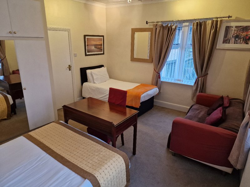 Spacious bedroom with two single beds, wooden table, sofa, and window with curtains