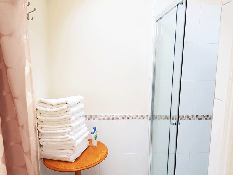 Bathroom with shower enclosure, stacked white towels on wooden table, and toiletries