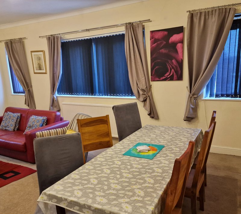 Spacious open-plan living and dining room with red sofa, dining table, and multiple windows with beige curtains