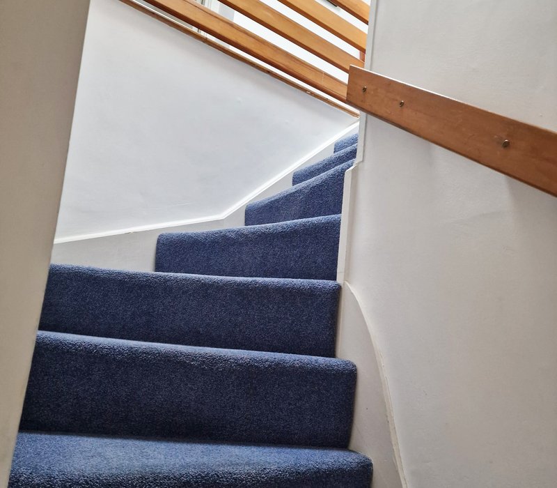 Staircase with dark blue carpet and wooden handrail leading upwards