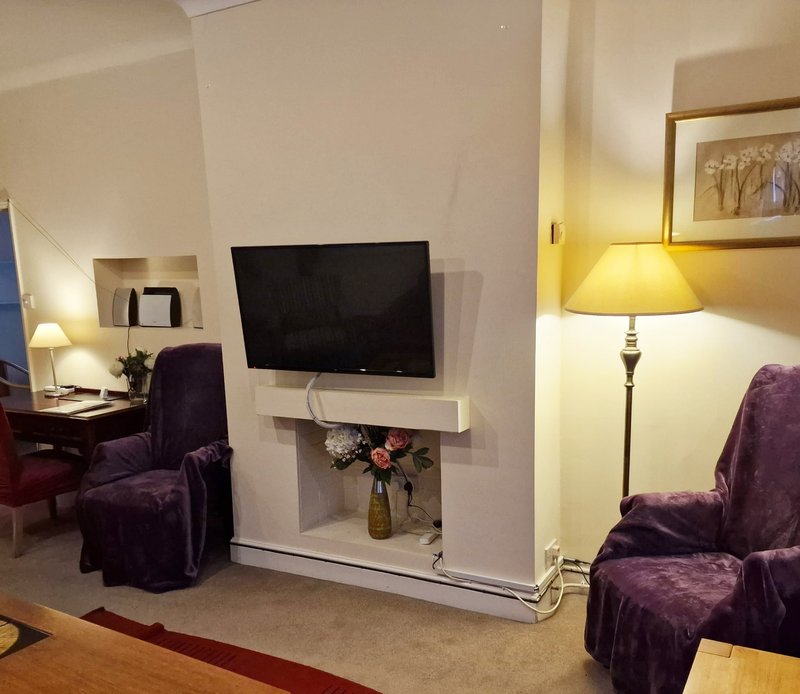 Living room with purple armchairs, wall-mounted TV, flowers in vase, and table lamps