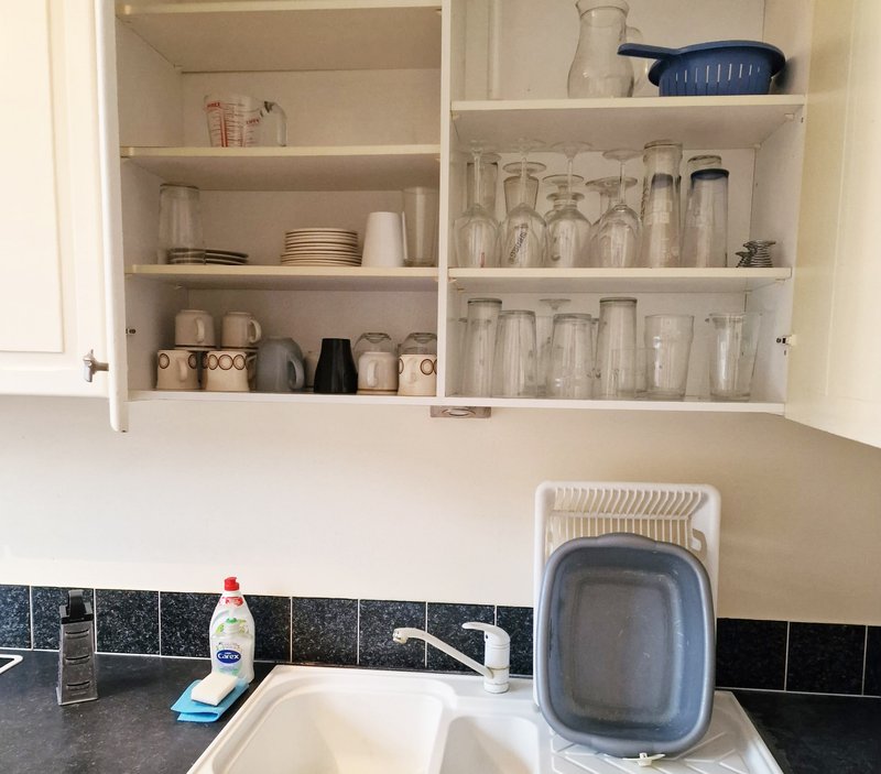 Kitchen sink with open shelving above displaying glassware, dishes, and household items