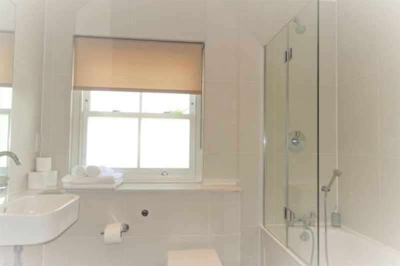 Clean modern bathroom with white sink, toilet, window, and glass shower enclosure